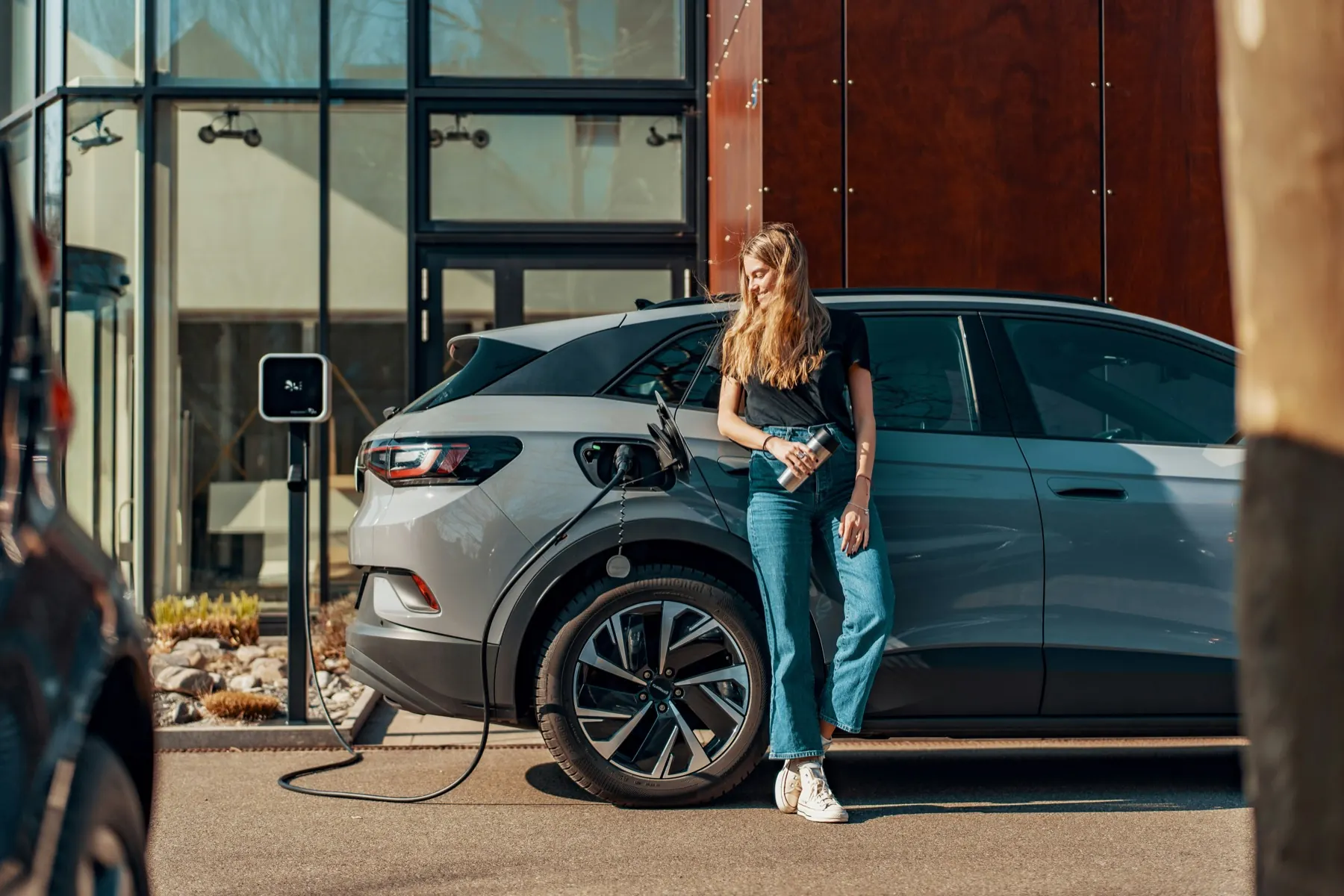 A driver standing beside an electric car plugged into a wall-mounted home charger